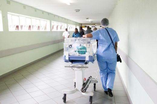 Pflegekraft geht mit einem Gerätewagen durch einen Krankenhausflur